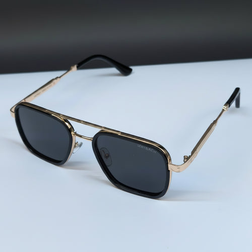 A pair of square aviator-style sunglasses with gold-tone metal frames, dark lenses, and black temple tips, resting on a white surface with a dark gray background.