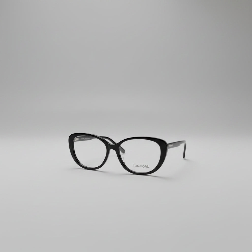 Black cat-eye eyeglasses with gold TOM FORD branding on the lower right lens, displayed on a clean white textured background.
