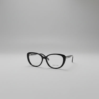 Black cat-eye eyeglasses with gold TOM FORD branding on the lower right lens, displayed on a clean white textured background.