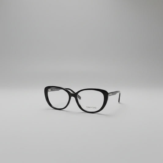 Black cat-eye eyeglasses with gold TOM FORD branding on the lower right lens, displayed on a clean white textured background.