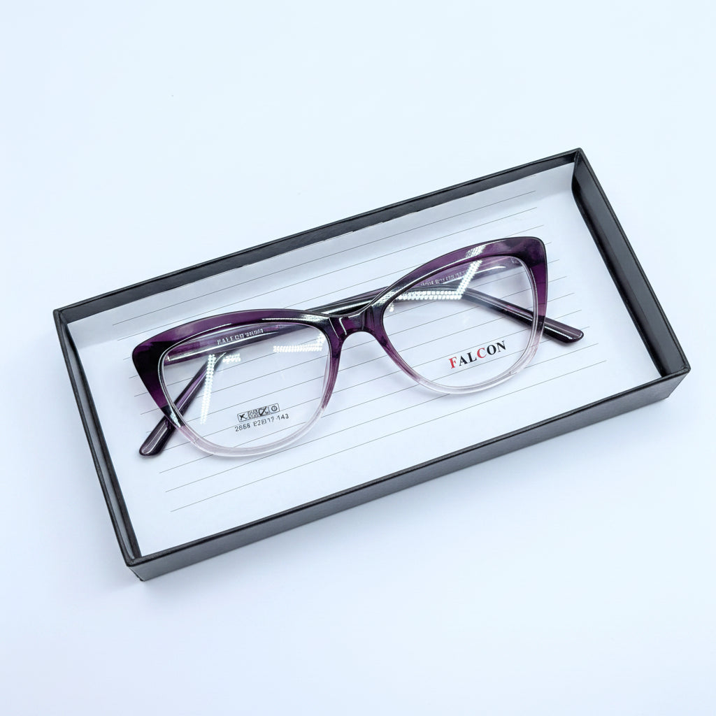 A pair of cat-eye eyeglasses with a purple-to-clear gradient acetate frame, resting inside a black presentation box on a white background.